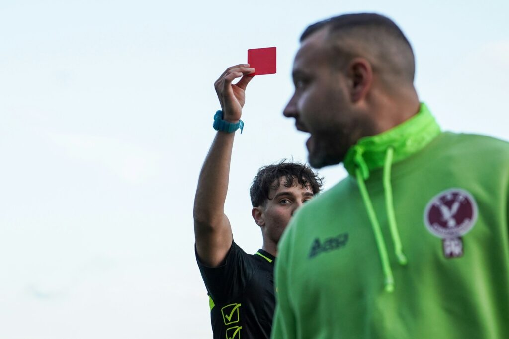 a referee holding a red card, showing one of the soccer card rules. Image by Alfonso Scarpa via www.unsplash.com