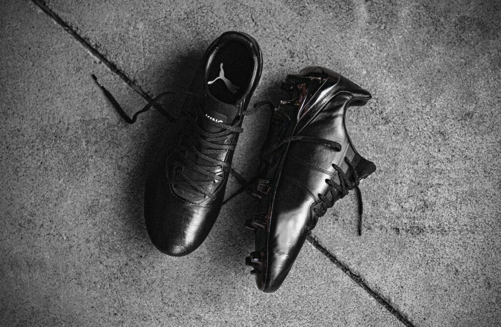 Black athletic footwear on concrete surface illustrating differences in design and traction for soccer cleats vs baseball cleats, highlighting studs, shape, and performance features. Image by Braden Hopkins via www.unsplash.com