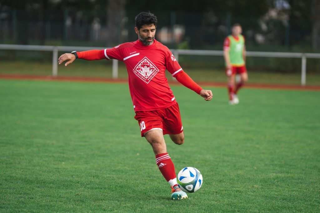 A soccer player kicking a ball on a field while wearing a red uniform featuring a centered team crest, demonstrating clear soccer jersey logo placement. Image by Omar Ramadan via www.unsplash.com
