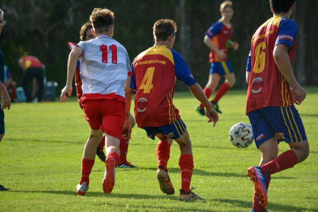 Young soccer players in action on a sunny field wearing high-performance kits, demonstrating why moisture-wicking is the best fabric for custom jersey comfort. Image by Talahria Jensen via www.unsplash.com